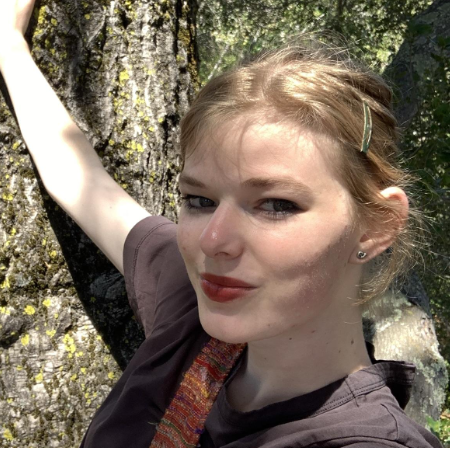 A person with blond hair pulled back looks at the camera with a slight smile