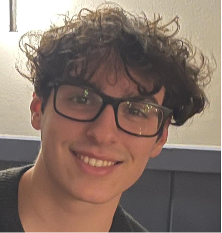 Photo of person with tousled brown hair wearing glasses looking at camera and smiling